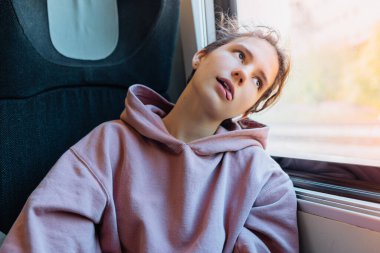 Uzun tren yolculuğundan sıkıldım. Modern sweatshirt 'lü genç kız, tren vagonunda tek başına oturur, sıkılır ve tembellikten suratını buruşturur.