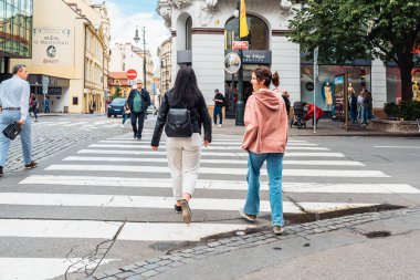 Küçük sırt çantalı iki genç bayan turist, Avrupa 'nın mimari manzarasına bakarak cadde boyunca yürüyorlar. Avrupa başkentinin orta kesimindeki yaya geçidi, turizm merkezi. Prag, Çek Cumhuriyeti, 05 2022