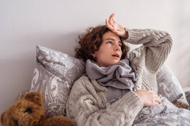 Genç bir kadın yatakta uzanıyor, elini alnında tutuyor, viral hastalık, titreme, grip, yüksek ateş. Battaniyenin altında kalın giysiler içinde hasta bir kadın baş ağrısı, migren, hastalık ve soğuk hisseder. Hasta ergen, negatif duygular, acı