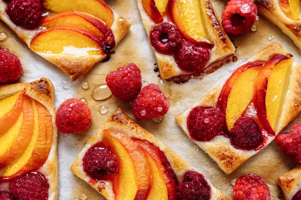 Fruit tartlets made from shortcrust pastry. Sweet fruit dessert cake, cut into portions, on baking paper, with a crispy crust and sweet raspberry and peach pieces. Side view, soft focus