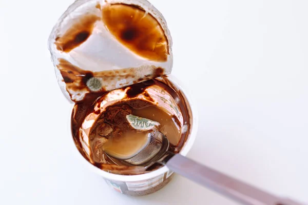chocolate mousse or moldy yogurt has expired. Moldy product in plastic cup with spoon inside on white isolated background. Top view. spoiled product in trash