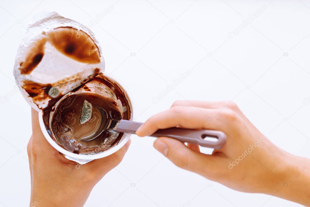 chocolate mousse or moldy yogurt has expired. woman's hands hold plastic cup with chocolate mousse or yogurt that has gone bad and moldy. Top view, white background