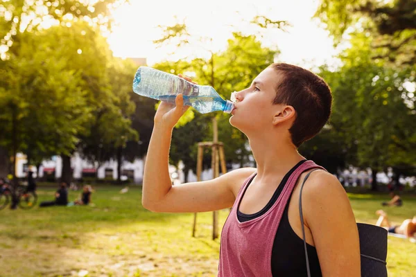 athletic teenage drinks sports isotonic from bottle after sports training, yoga, ina public park, sunset. Healthy lifestyle, sports, outdoor fitness. Useful training, athletic physique, strong muscles.