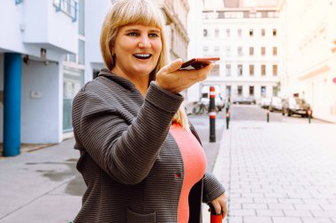 Olgun, orta yaşlı, 40 'lı yaşlarda, uzun sarı saçlı, gülümseyen, kot giyen, örgü ören, akıllı telefon kullanan, video görüşmesinde konuşan bir kadın.