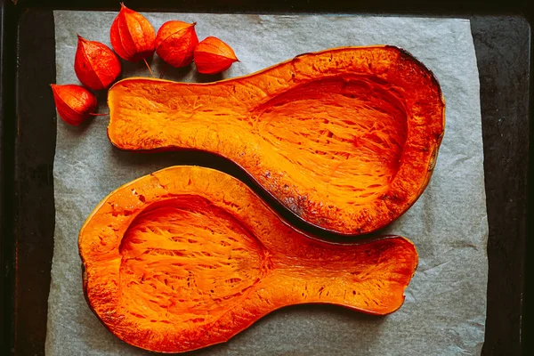 Baked pear-shaped Butternut pumpkin cut into two symmetrical halves, on baking sheet. Vegetarian baked rustic food, bright orange vegetable, pumpkin soup ingredient