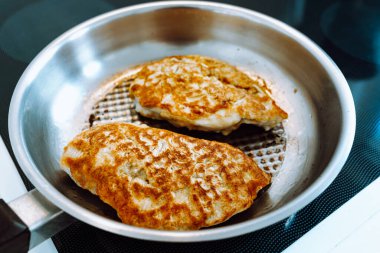 Fried chicken breast in batter and breadcrumbs in grill pan, cooking Austrian schnitzel. Grilled meat with crispy crust in batter in pan, soft focus, delicious appetizing lunch or dinner