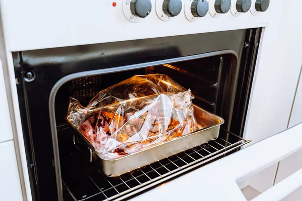 Cooking meat in plastic bag for baking. no plastic concept. Fresh mutton or beef meat packed in spice sleeve ready to bake, seen through open oven door. Festive dinner, healthy food without vegetable fat and frying