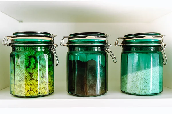 storage of products in eco packaged glass jar. Three green glass jars with glass lid filled with bulk products, cereals, rice, pasta and coffee stand on shelf in row