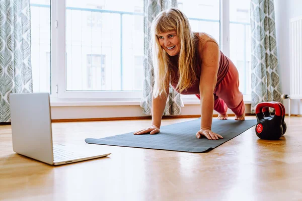 middle-aged woman with curvaceous, plump, blonde, standing in plank position, doing yoga, sports, at home oline. Active lifestyle, keeping body in good shape for middle-aged women
