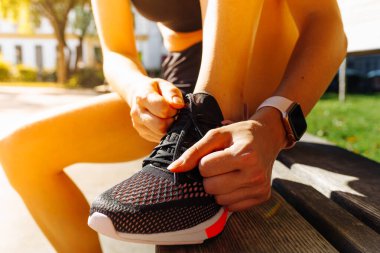 Spor ayakkabılı, spor ayakkabılı, spor şortlu, kalite kontrolü için elektronik saati olan bir kızın kaslı bacakları. Spor ayakkabılarına basamaklı ayakkabı bağcığı takan bir sporcu elleri. çalışma ekipmanı kavramı.