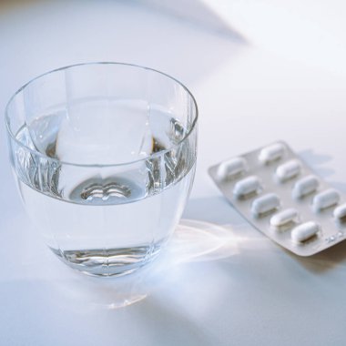 Işık huzmelerinde bir bardak temiz su ve hapların üzerinde haplar. Aspirin hapları, parasetamol, ibuprofen ve bir bardak su, yaşam tarzı, hastalık, sağlık