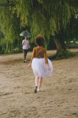 Kharkiv, Ukrayna. 09.19.2021. Şiddetli yağmurda şemsiyeyle nehrin kenarında yürüyen komik bir çiftin aşk hikayesi. Beyaz etekli, sarı kazaklı hoş bir adam ve kadın. Aile tatili ve birliktelik, randevu