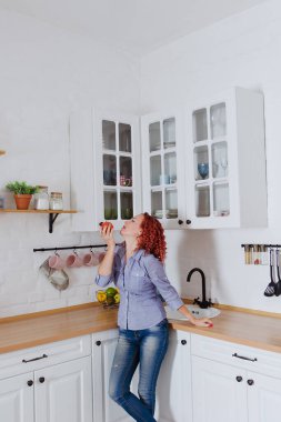 Genç, kızıl saçlı, kıvırcık saçlı, 30 'lu yaşlarda kot pantolonlu ve temiz mutfağında oturan ve rahatlatıcı gömleği olan bir kadın. Sağlıklı ve mutlu bir yaşam tarzı. Boş zaman. Ev hanımı.. 