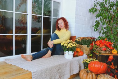 Güzel kızıl saçlı, kıvırcık saçlı, sıcak kazaklı bir kadın rahat bir evde yatakta oturuyor, gülüyor, eğleniyor. Sonbahar süslemeleri, portakal yaprakları, çiçekler, balkabakları olan ev.. 