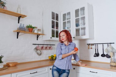 Genç, kızıl saçlı, kıvırcık saçlı, 30 'lu yaşlarda kot pantolonlu ve temiz mutfağında oturan ve rahatlatıcı gömleği olan bir kadın. Sağlıklı ve mutlu bir yaşam tarzı. Boş zaman. Ev hanımı.. 