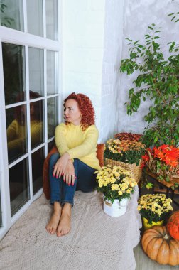 Güzel kızıl saçlı, kıvırcık saçlı, sıcak kazaklı bir kadın rahat bir evde yatakta oturuyor, gülüyor, eğleniyor. Sonbahar süslemeleri, portakal yaprakları, çiçekler, balkabakları olan ev.. 