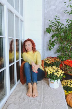 Güzel kızıl saçlı, kıvırcık saçlı, sıcak kazaklı bir kadın rahat bir evde yatakta oturuyor, gülüyor, eğleniyor. Sonbahar süslemeleri, portakal yaprakları, çiçekler, balkabakları olan ev.. 