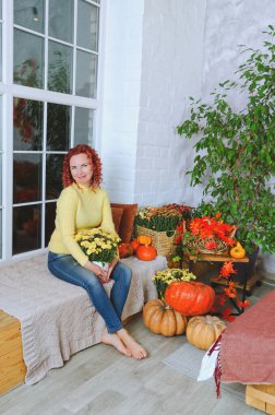 Güzel kızıl saçlı, kıvırcık saçlı, sıcak kazaklı bir kadın rahat bir evde yatakta oturuyor, gülüyor, eğleniyor. Sonbahar süslemeleri, portakal yaprakları, çiçekler, balkabakları olan ev.. 