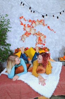 İki hoş genç kadın, kız kardeş, sıcak kazaklı arkadaşlar rahat bir evde yatakta oturmuş gülüyor, eğleniyorlar. Sonbahar süslemeleri, portakal yaprakları, çiçekler, balkabakları olan ev.. 