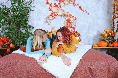 İki hoş genç kadın, kız kardeş, sıcak kazaklı arkadaşlar rahat bir evde yatakta oturmuş gülüyor, eğleniyorlar. Sonbahar süslemeleri, portakal yaprakları, çiçekler, balkabakları olan ev.. 