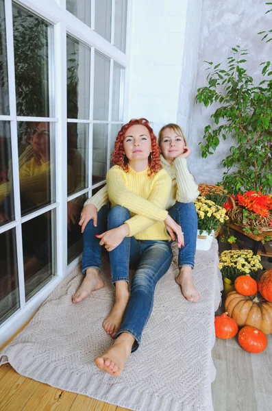 İki hoş genç kadın, kız kardeş, sıcak kazaklı arkadaşlar rahat bir evde yatakta oturmuş gülüyor, eğleniyorlar. Sonbahar süslemeleri, portakal yaprakları, çiçekler, balkabakları olan ev.. 