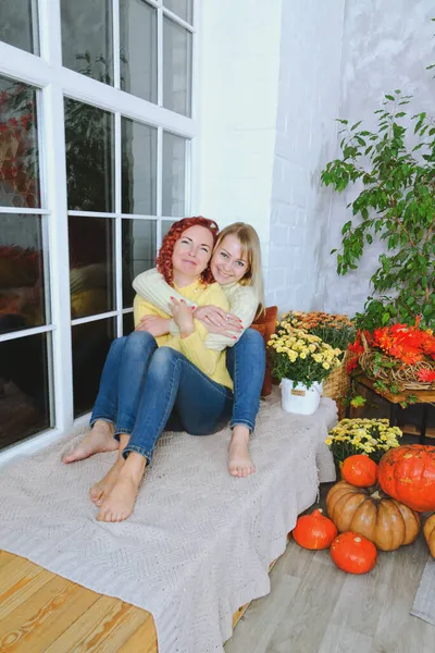 İki hoş genç kadın, kız kardeş, sıcak kazaklı arkadaşlar rahat bir evde yatakta oturmuş gülüyor, eğleniyorlar. Sonbahar süslemeleri, portakal yaprakları, çiçekler, balkabakları olan ev.. 