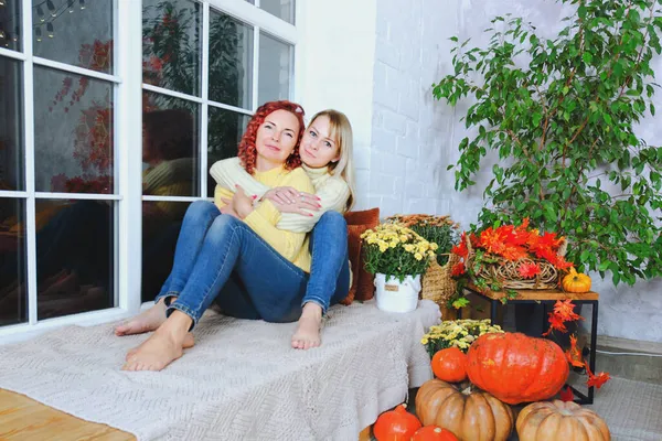 İki hoş genç kadın, kız kardeş, sıcak kazaklı arkadaşlar rahat bir evde yatakta oturmuş gülüyor, eğleniyorlar. Sonbahar süslemeleri, portakal yaprakları, çiçekler, balkabakları olan ev.. 