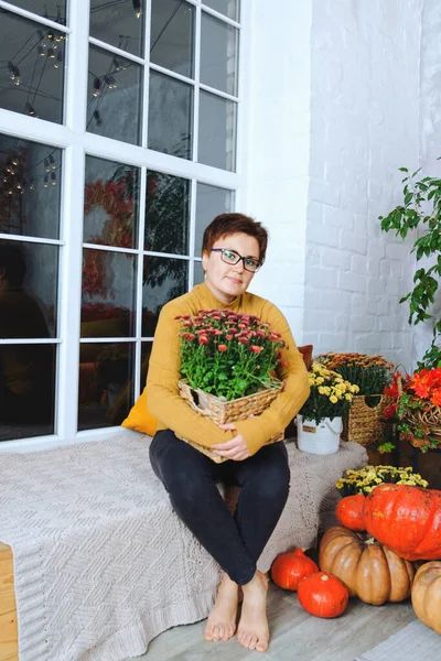 young woman with short hair sitting in her cozy bad in yellow sweater in cold fall day. Home interior design, autumn decorations and pumpkins.