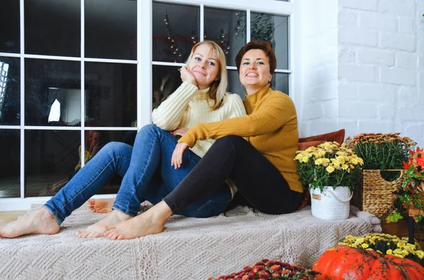 İki hoş genç kadın, kız kardeş, sıcak kazaklı arkadaşlar rahat bir evde yatakta oturmuş gülüyor, eğleniyorlar. Sonbahar süslemeleri, portakal yaprakları, çiçekler, balkabakları olan ev.. 