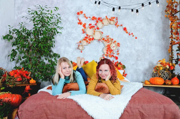 İki hoş genç kadın, kız kardeş, sıcak kazaklı arkadaşlar rahat bir evde yatakta oturmuş gülüyor, eğleniyorlar. Sonbahar süslemeleri, portakal yaprakları, çiçekler, balkabakları olan ev.. 