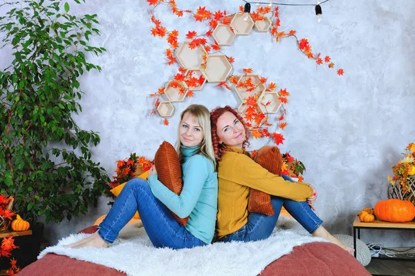 İki hoş genç kadın, kız kardeş, sıcak kazaklı arkadaşlar rahat bir evde yatakta oturmuş gülüyor, eğleniyorlar. Sonbahar süslemeleri, portakal yaprakları, çiçekler, balkabakları olan ev.. 