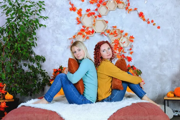 İki hoş genç kadın, kız kardeş, sıcak kazaklı arkadaşlar rahat bir evde yatakta oturmuş gülüyor, eğleniyorlar. Sonbahar süslemeleri, portakal yaprakları, çiçekler, balkabakları olan ev.. 