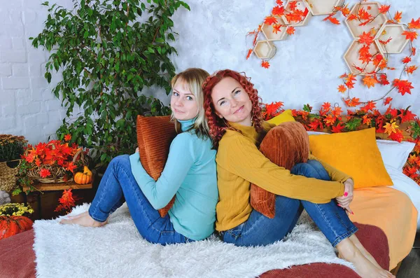 İki hoş genç kadın, kız kardeş, sıcak kazaklı arkadaşlar rahat bir evde yatakta oturmuş gülüyor, eğleniyorlar. Sonbahar süslemeleri, portakal yaprakları, çiçekler, balkabakları olan ev.. 