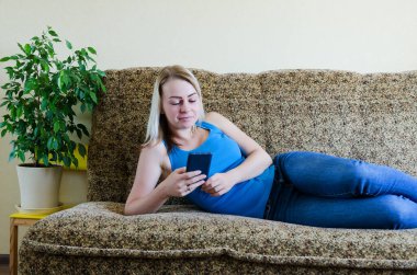 Evdeki genç sarışın kadın kanepede oturuyor, rahatla. Evden cep telefonuyla çalışıyorum. Mutlu aile hayatı, hobi ve boş zaman. İş kadını kavramı