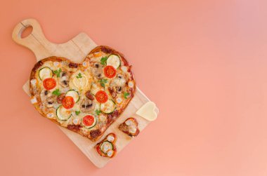 Arka planda Sevgililer Günü için domatesli, sebzeli ve peynirli kalp şeklinde pizza. Romantik aşkın yaratıcı yemek konsepti. Üst manzara, düz uzanma.