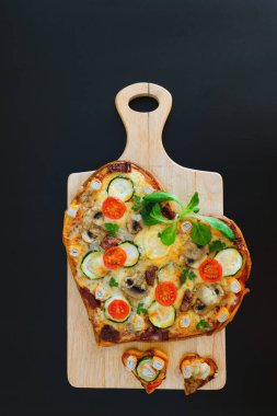 Arka planda Sevgililer Günü için domatesli, sebzeli ve peynirli kalp şeklinde pizza. Romantik aşkın yaratıcı yemek konsepti. Üst manzara, düz uzanma.