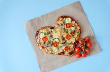 Arka planda Sevgililer Günü için domatesli, sebzeli ve peynirli kalp şeklinde pizza. Romantik aşkın yaratıcı yemek konsepti. Üst manzara, düz uzanma.