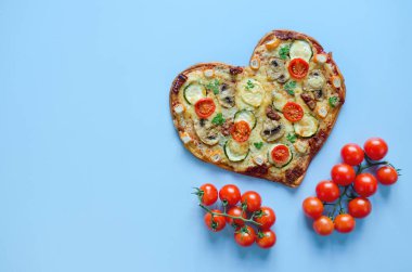 Arka planda Sevgililer Günü için domatesli, sebzeli ve peynirli kalp şeklinde pizza. Romantik aşkın yaratıcı yemek konsepti. Üst manzara, düz uzanma.