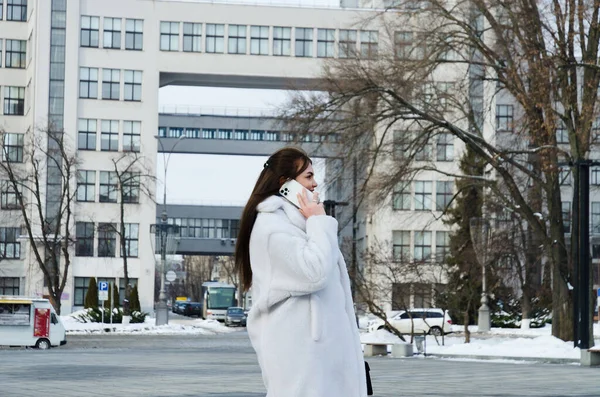 都市的年轻优雅的女商人穿着冬季休闲装 白色夹克 在城市街道上散步 在电话里聊天 自私自利 室外工作 — 图库照片