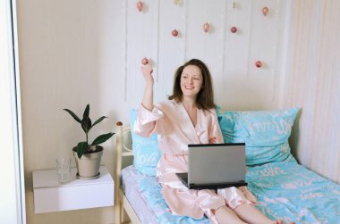 Genç mutlu iş kadını rahat bir evde pijamalarıyla yatar. İnternette çalışıyor, laptopla evde ders çalışıyor. Serbest çalışan biri. Sabah ritüelleri. 