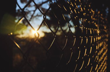 Geometrik bir kafesin dokusu, çit, arka planda kırmızı bir günbatımı gökyüzünün duvarı. Soyut sanat. Bokeh