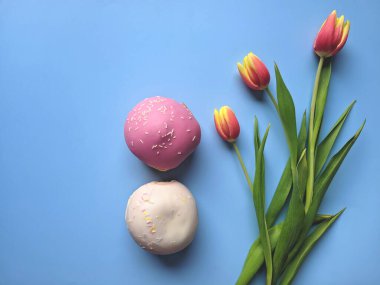 Bir fincan sıcak kahve ve mavi arka planda tatlı çöreklerle dolu bir sabah. Bir buket lale. Üst görünüm, kopyalama alanı, modelleme. Düz yatıyordu. Yiyecek ve içecekler. Bahar tatili. 