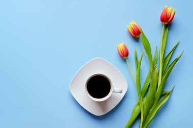 Bir fincan sıcak kahve ve mavi arka planda tatlı çöreklerle dolu bir sabah. Bir buket lale. Üst görünüm, kopyalama alanı, modelleme. Düz yatıyordu. Yiyecek ve içecekler. Bahar tatili. 