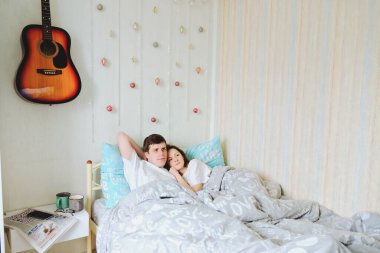 Mutlu çift sıcak bir evde yatakta uzanıyor, kahve içiyor. Tişörtlü genç bir adam ve hoş bir kadın. Aile tatili ve birliktelik, aşkım. Hafta sonu. Yaşam biçimi.