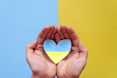 Ukrayna bayrağını tutan insan elleri, sarı ve mavi arka planda izole edilmiş kalbi gösteriyor. Yardım, destek ve Ukrayna 'da savaş olmaması kavramının sembolü