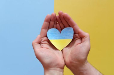 Ukrayna bayrağını tutan insan elleri, sarı ve mavi arka planda izole edilmiş kalbi gösteriyor. Yardım, destek ve Ukrayna 'da savaş olmaması kavramının sembolü