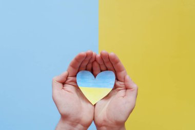 Ukrayna bayrağını tutan insan elleri, sarı ve mavi arka planda izole edilmiş kalbi gösteriyor. Yardım, destek ve Ukrayna 'da savaş olmaması kavramının sembolü