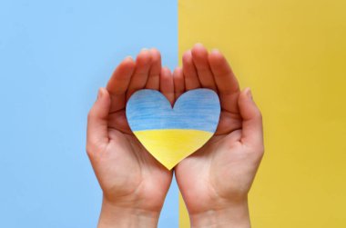 Ukrayna bayrağını tutan insan elleri, sarı ve mavi arka planda izole edilmiş kalbi gösteriyor. Yardım, destek ve Ukrayna 'da savaş olmaması kavramının sembolü