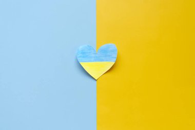 Ukrayna bayrağını tutan insan elleri, sarı ve mavi arka planda izole edilmiş kalbi gösteriyor. Yardım, destek ve Ukrayna 'da savaş olmaması kavramının sembolü