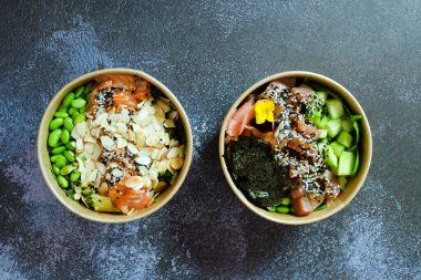 Tava kutusunun üst görüntüsü, siyah arka planda bir kase pirinç. Somon, avokado, soğan, mantar, brokoli ve susamlı pilav. Çin, Asya yemeği teslimatı. Tavalar için ambalaj. 